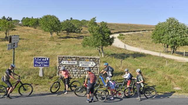 Cyclistes au Col des Supeyres, altitude 1336m, entourés de paysages naturels avec clôtures, arbres et ciel dégagé.