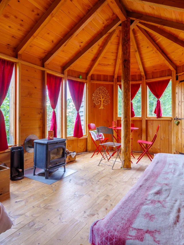 Intérieur de la Cabane des Colibris à Sauvessanges, avec une grande chambre, un poêle à bois, et un coin salon chaleureux.