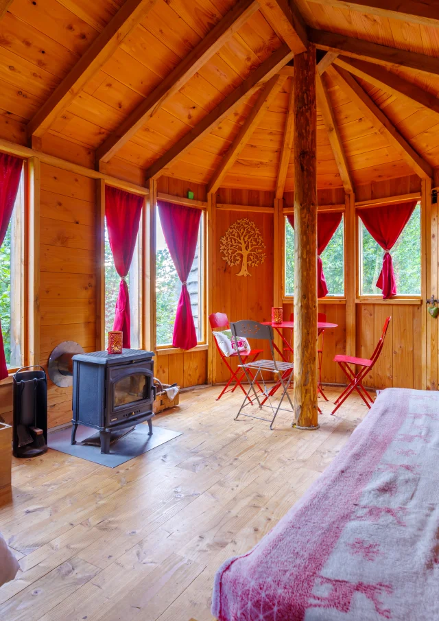 Intérieur de la Cabane des Colibris à Sauvessanges, avec une grande chambre, un poêle à bois, et un coin salon chaleureux.