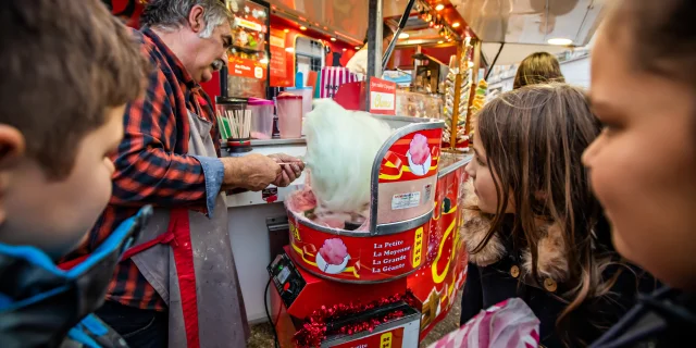 Un marchand prépare une barbapapa pour des enfants, au stand sucré du marché de Noël de Thiers.