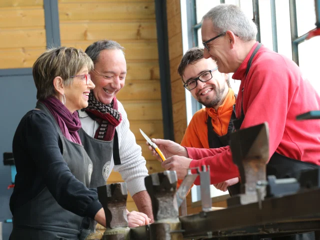 Un couple en discussion avec des artisans à la coutellerie Robert David à Thiers, l’un présentant un couteau artisanal.