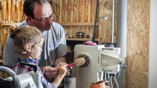 Un artisan du Cœur de Bois à Thiers explique les techniques de travail du bois à une petite fille, tout en lui présentant l’une des machines utilisées dans la fabrication artisanale