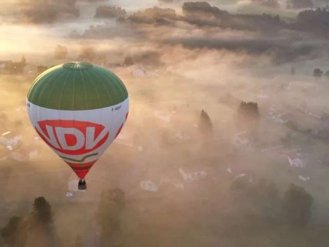 Montgolfière au-dessus d’un paysage de brume à Viverols, dans la Vallée de l'Ance, avec des habitations visibles.