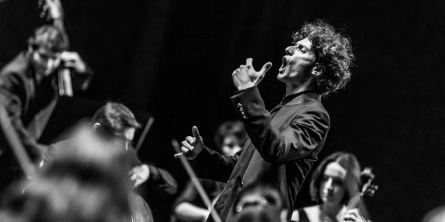 Chanteur en pleine prestation, entouré de musiciens, lors du Festival Arioso – Nuits Classiques de Thiers, image en noir et blanc.