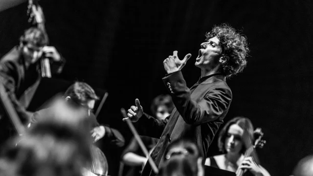 Chanteur en pleine prestation, entouré de musiciens, lors du Festival Arioso – Nuits Classiques de Thiers, image en noir et blanc.