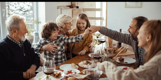 Illustration d’un repas de Noël en famille avec une grand-mère souriante entourée d’enfants, un grand-père et des parents autour d’une table festive en bois.