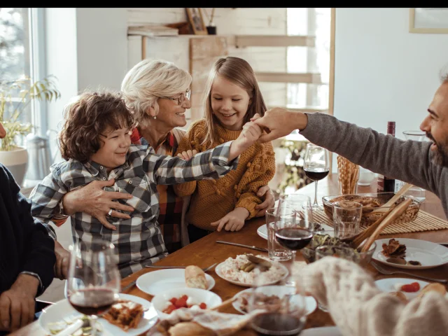 Illustration d’un repas de Noël en famille avec une grand-mère souriante entourée d’enfants, un grand-père et des parents autour d’une table festive en bois.