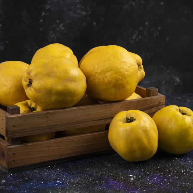 Des coings frais, soigneusement disposés dans une cagette en bois, prêts à être utilisés dans la recette des rœsti de panais et de coing avec chutney.