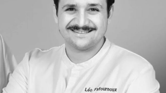 Portrait en noir et blanc de Léo Fournoux, chef cuisinier, bras croisés, portant un tablier brodé des couleurs des Toques d'Auvergne, extrait de l’émission Grands Reportages sur TF1.