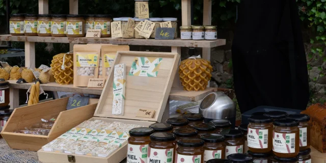 Stand de miel avec des pots, du nougat, du pain d'épices et des bougies, sur un marché artisanal.