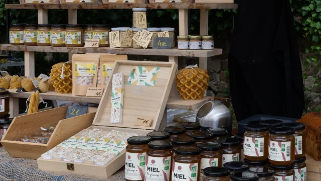 Stand de miel avec des pots, du nougat, du pain d'épices et des bougies, sur un marché artisanal.