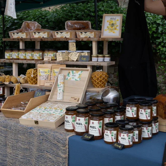 Stand de miel avec des pots, du nougat, du pain d'épices et des bougies, sur un marché artisanal.