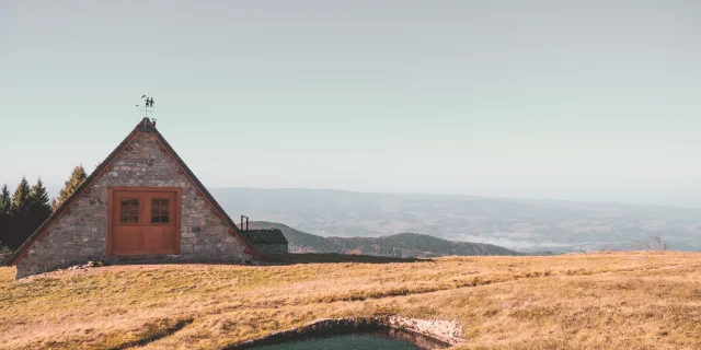 Paysage du Col des Supeyres avec une petite bâtisse en pierre, une mare d'altitude et une vue dégagée sur les montagnes et vallées environnantes.